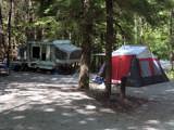 A camping trailer and a tent are set up among the trees at the Warsaw Caves Conservation Area campsite